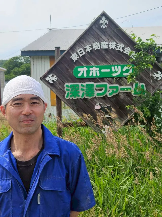 オホーツク深澤ファームの看板前に立つスタッフ